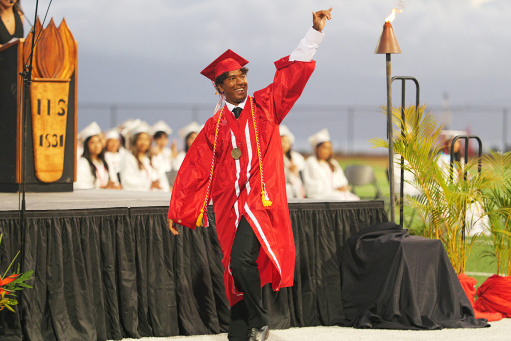 High school student giving a shaka while walking across the stage during graduation ceremony