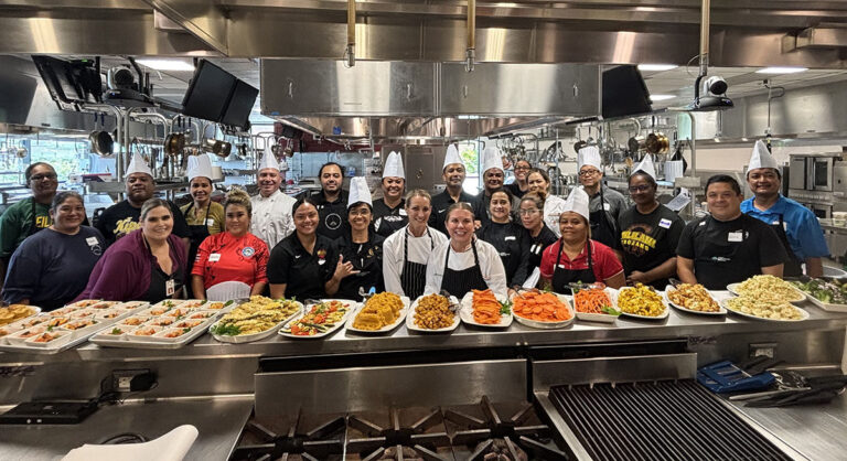 A group photo is taken inside of a kitchen.