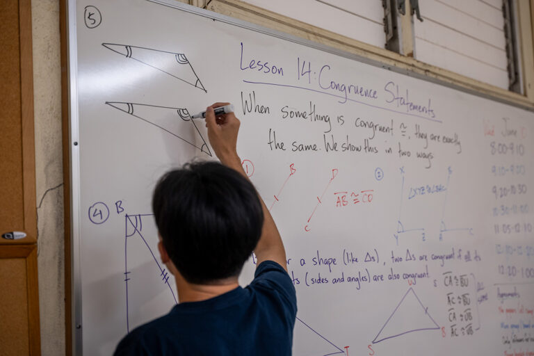 A teacher demonstrates a math problem on the whiteboard in front of the class.