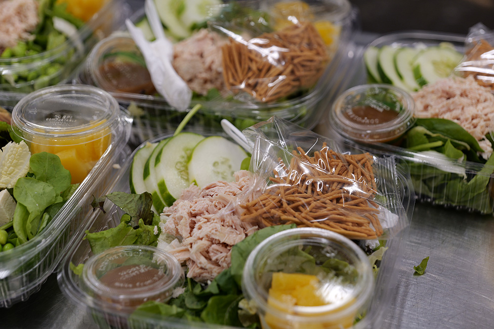 Trays of Chinese Chicken Salad are plated with greens, chicken, cucumbers and fruit.