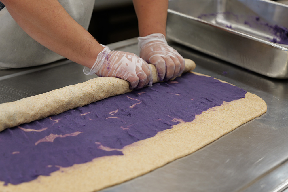 A baker rolls dough to make ʻuala swirl bun.