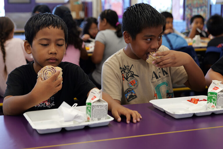 Two students eat ʻuala swirl buns in the cafeteria.
