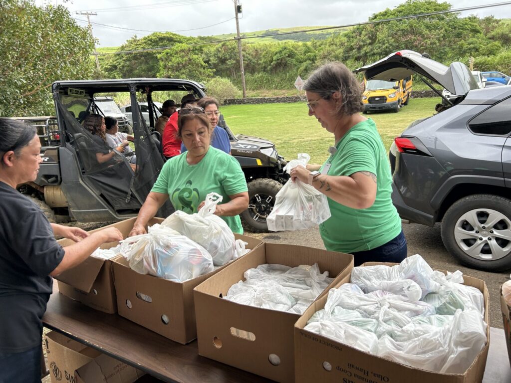 Two women carry food to a car.