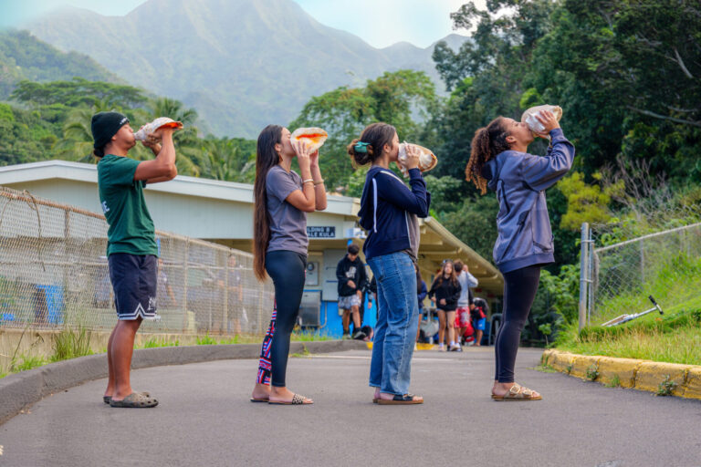 Four students blowing into conch shells