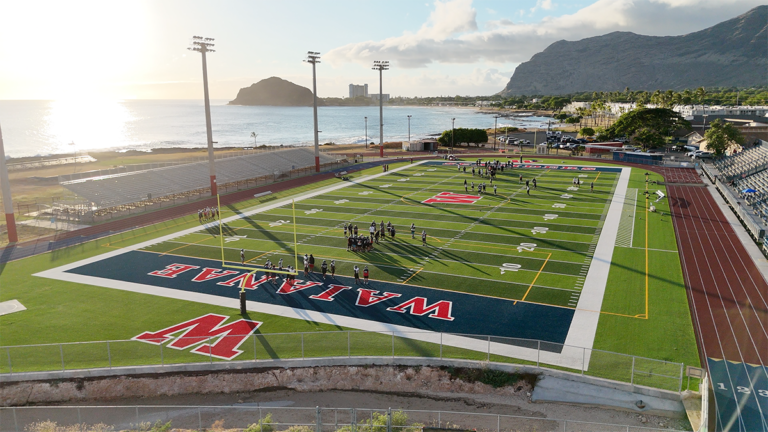 Students practice on the Wai‘anae High football field with the mountains and ocean in the background.