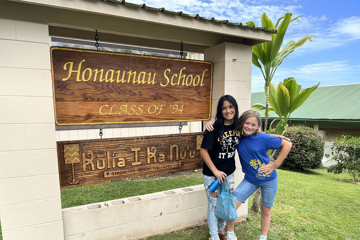 two students in standing next to school sign