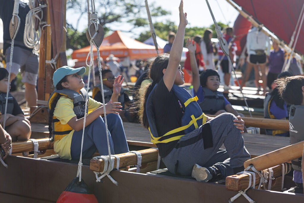 Students raise their hands while sitting in a canoe.