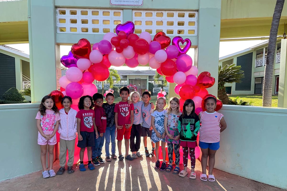 students standing under red and pink balloons